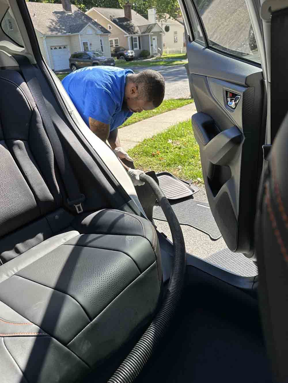 a man is cleaning the back seat of a car with a vacuum cleaner .