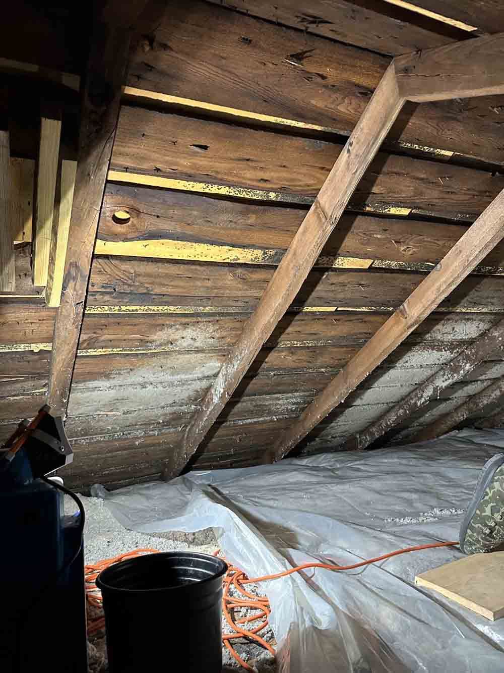 an attic with wooden beams and a plastic tarp on the floor .