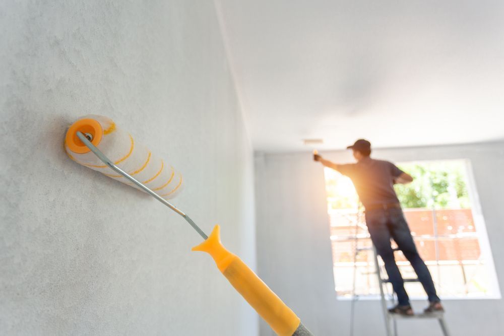 a man is standing on a ladder painting a wall with a paint roller .