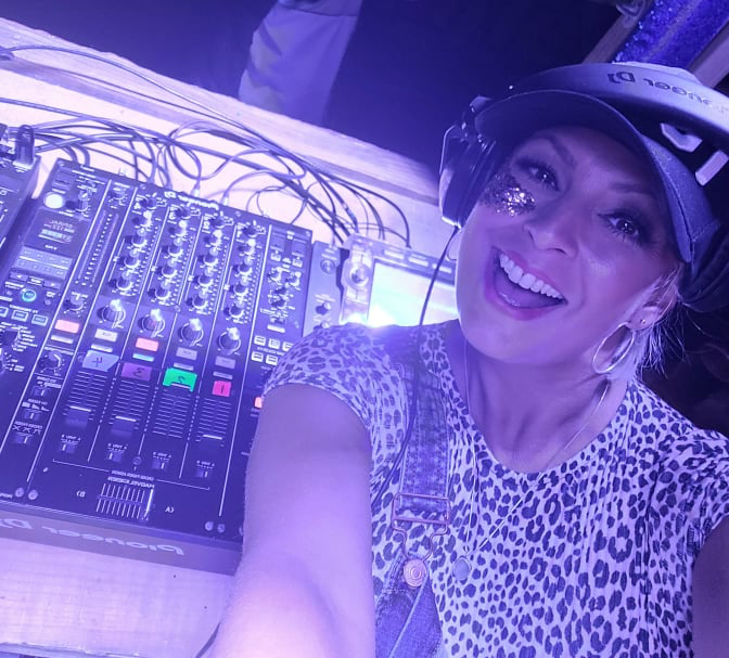 A woman wearing headphones and a hat is smiling in front of a mixer.