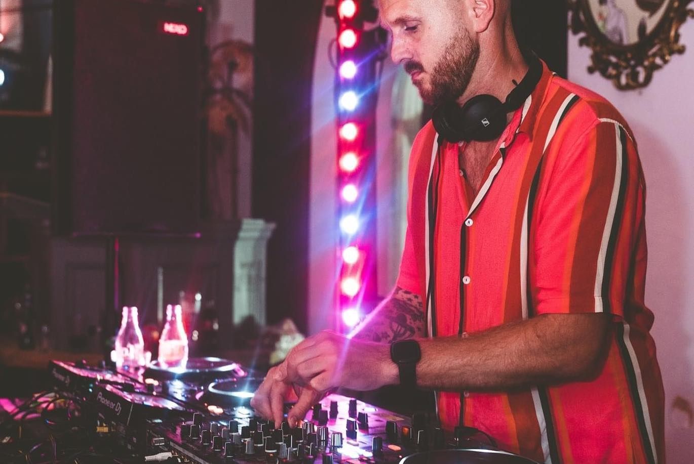 A man in a red striped shirt is playing music on a dj mixer.