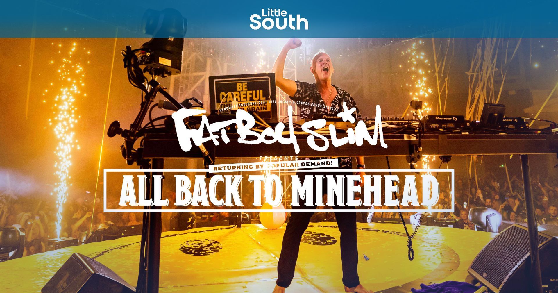 A man is standing on a stage with the words all back to minehead above him