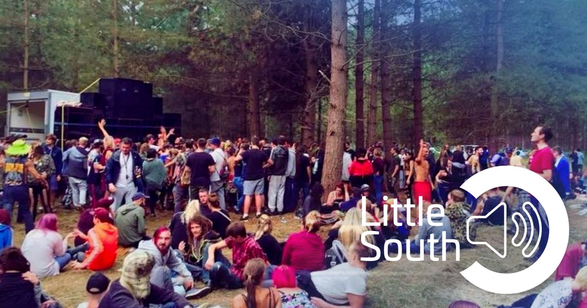 A large group of people are gathered in the woods at a little south festival.