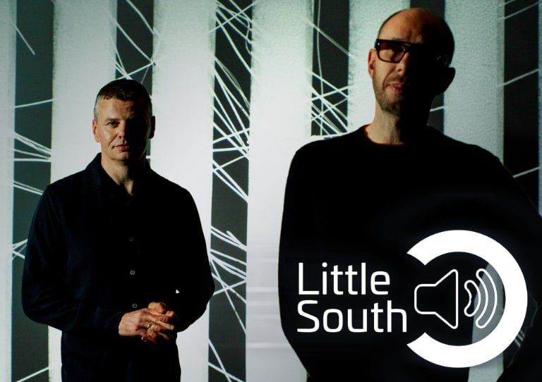 Two men are standing next to each other in front of a sign that says little south