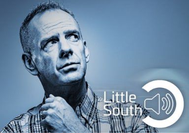 A man in a plaid shirt is looking up with a little south logo in the background