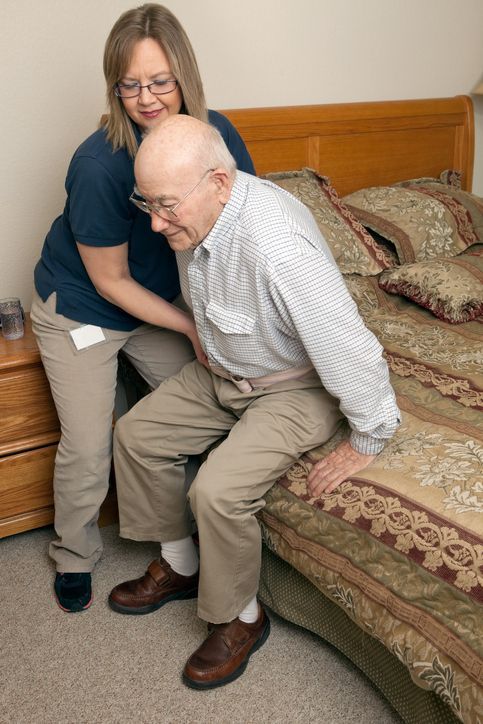 A woman is helping an elderly man get out of bed.