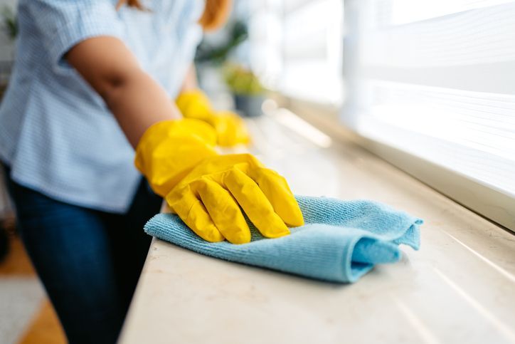 A woman wearing yellow gloves is cleaning a counter with a cloth.