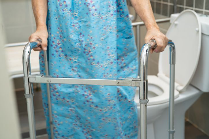 A woman in a blue dress is using a walker to go to the toilet.