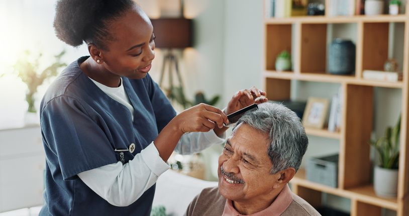 A nurse is brushing a man 's hair in a living room.