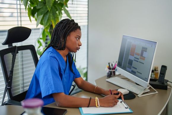 A nurse is sitting at a desk in front of a computer.