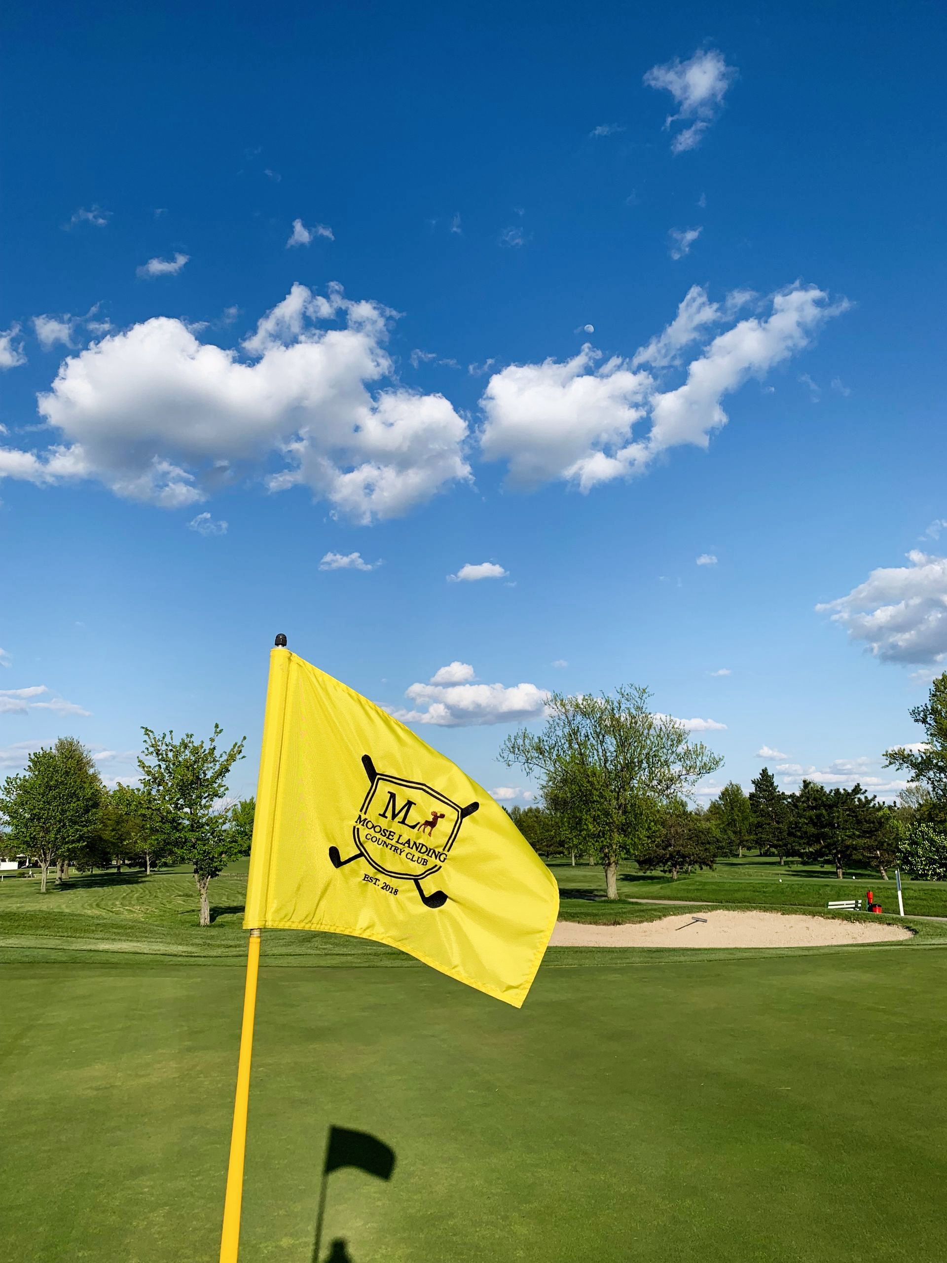 A yellow flag is flying in the wind on a golf course.