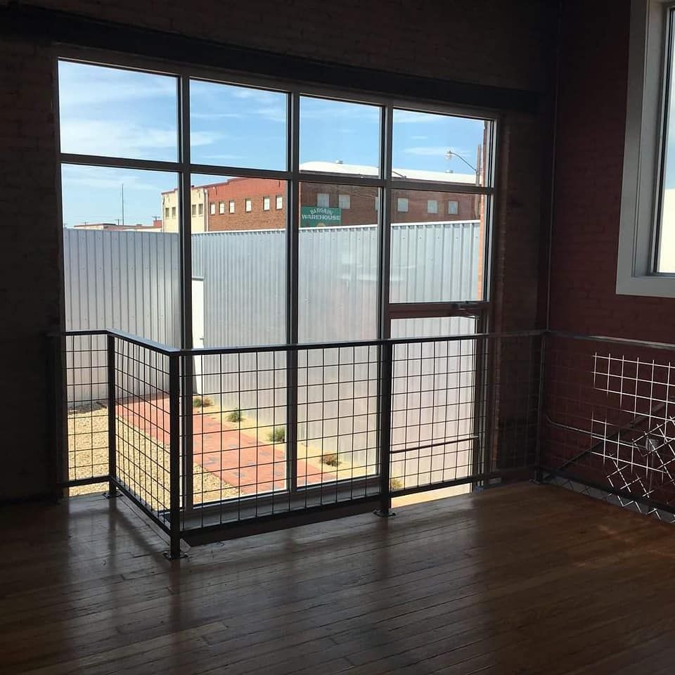 Interior view with large windows, metal railing, brick wall, and view of a street with buildings.