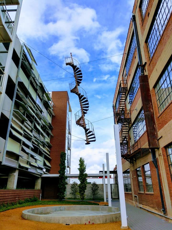 Suspended spiral staircases between brick buildings against a cloudy blue sky.