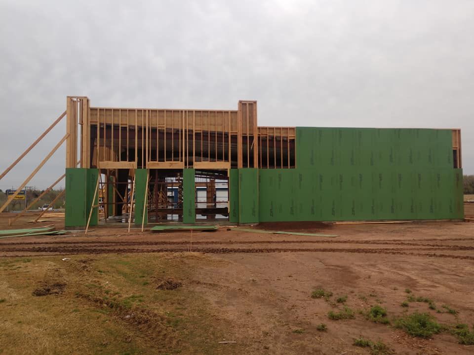 Building under construction with wooden frame and green siding on a dirt lot under an overcast sky.