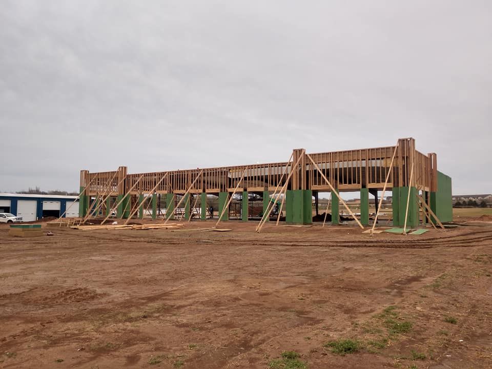 Construction site with wooden framing, braced with supports, on brown dirt under a cloudy sky.