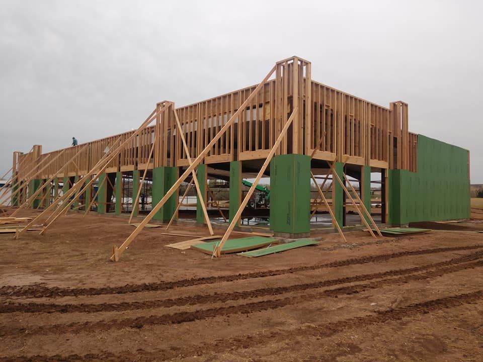 Construction site with wooden framing and green exterior wall panels, supported by bracing.