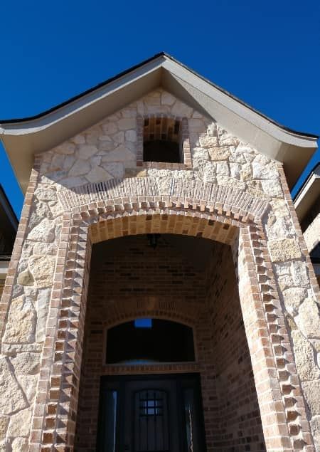 Stone and brick arched entryway of a house against a clear blue sky.