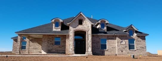 Stone-and-brick house with a dark roof against a clear blue sky.