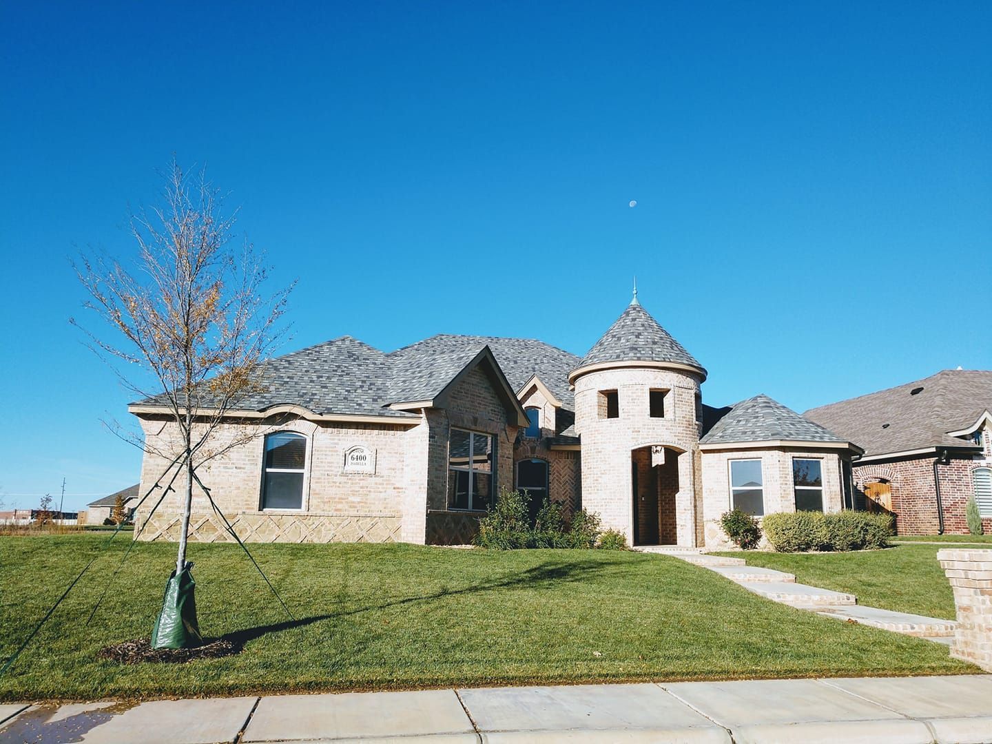 Beige brick house with turret, green lawn, blue sky.