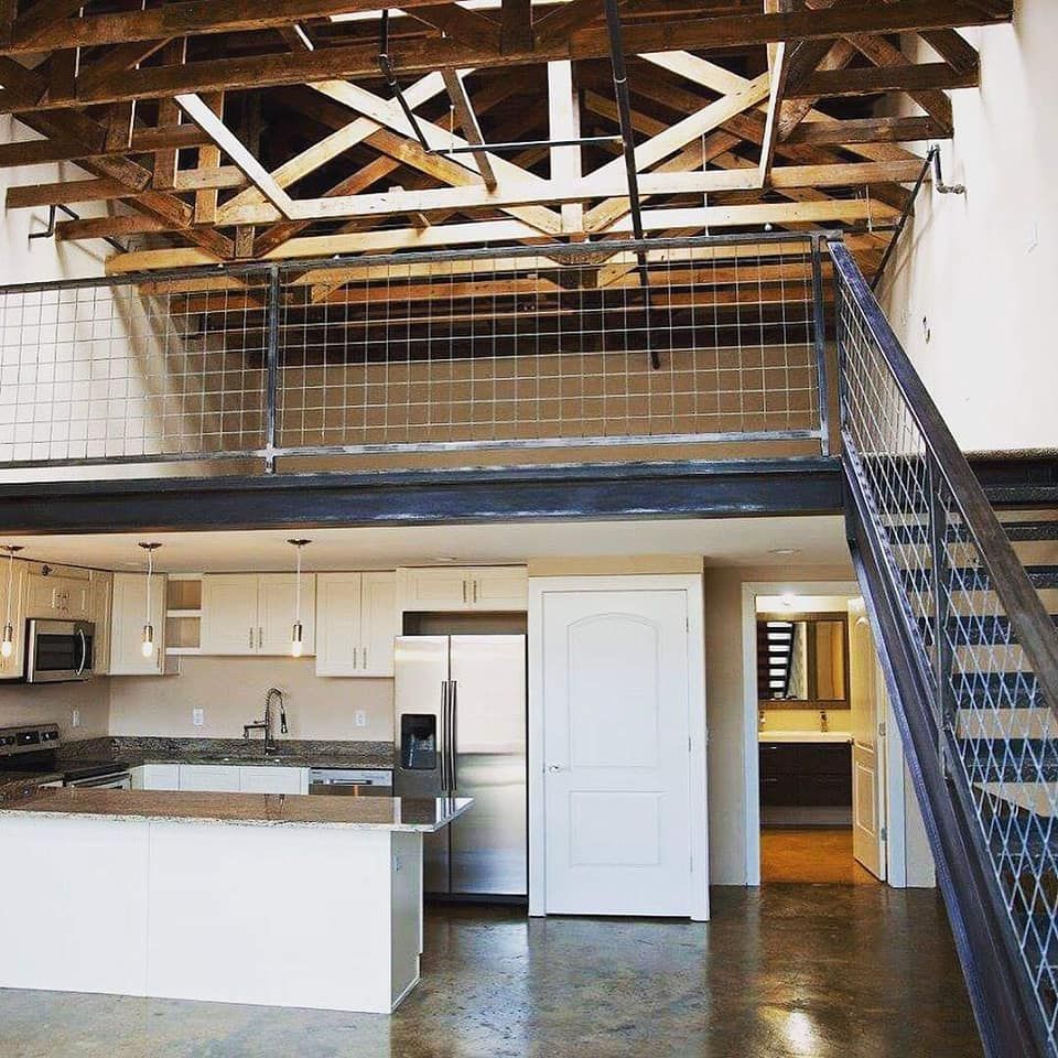 Modern loft interior with a kitchen, exposed beams, and a metal staircase leading to a lofted area.