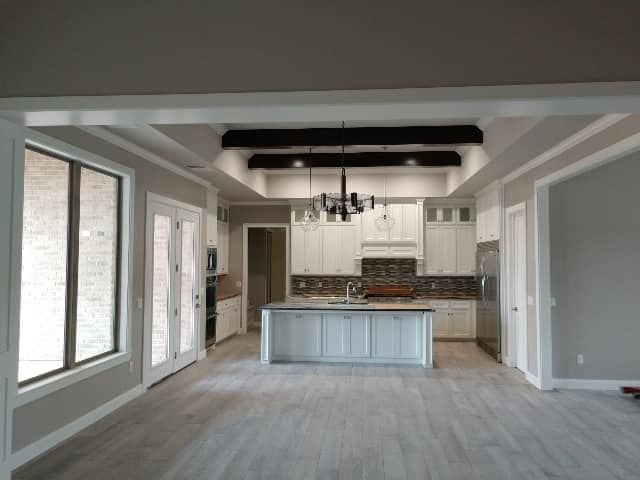 Open-concept kitchen with white cabinets, island, and ceiling beams.