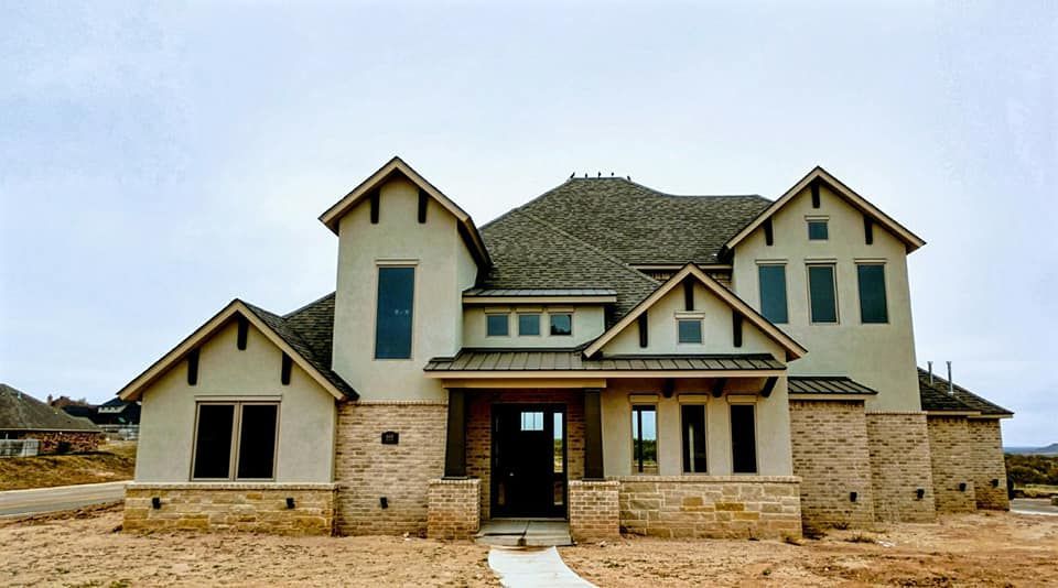 Newly constructed house with tan stucco, brick accents, and a brown roof.