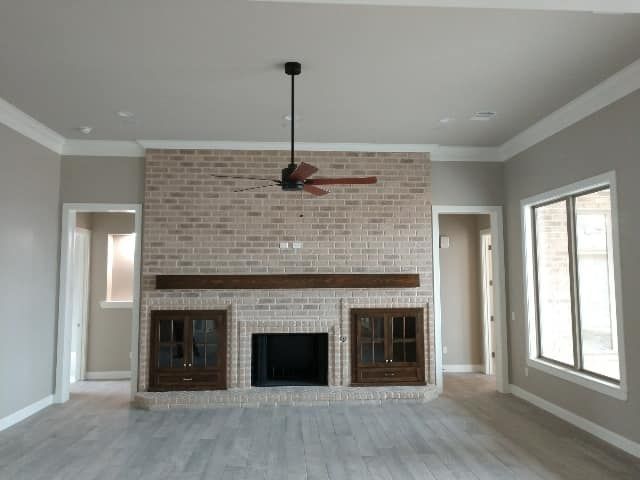 Living room with light brick fireplace, brown mantle, ceiling fan, and gray walls.