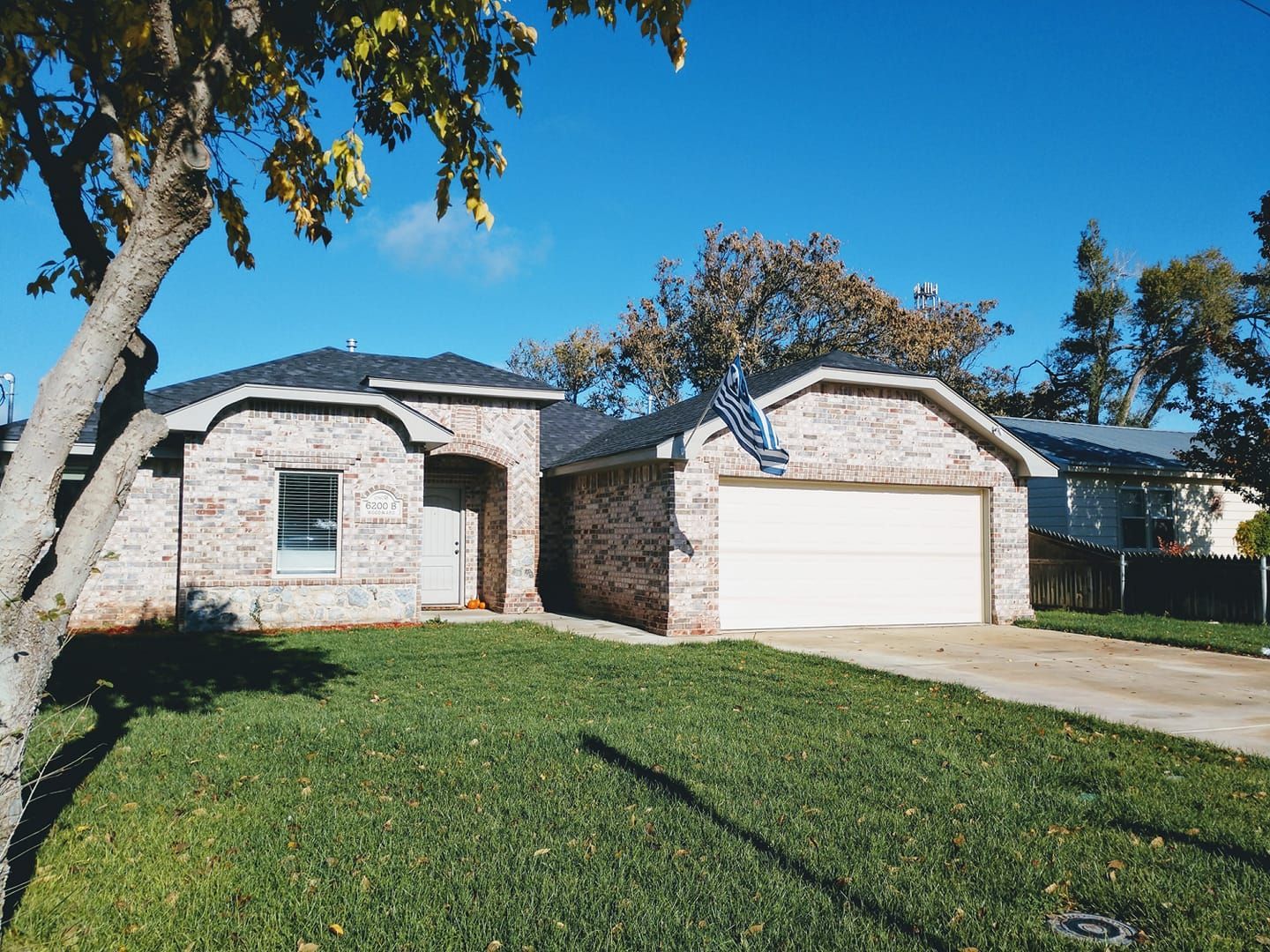 Brick house with attached garage, green lawn, tree with yellow leaves under a blue sky.