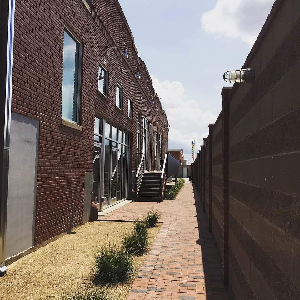 Brick buildings flank a narrow brick walkway with a wooden fence on the right. 