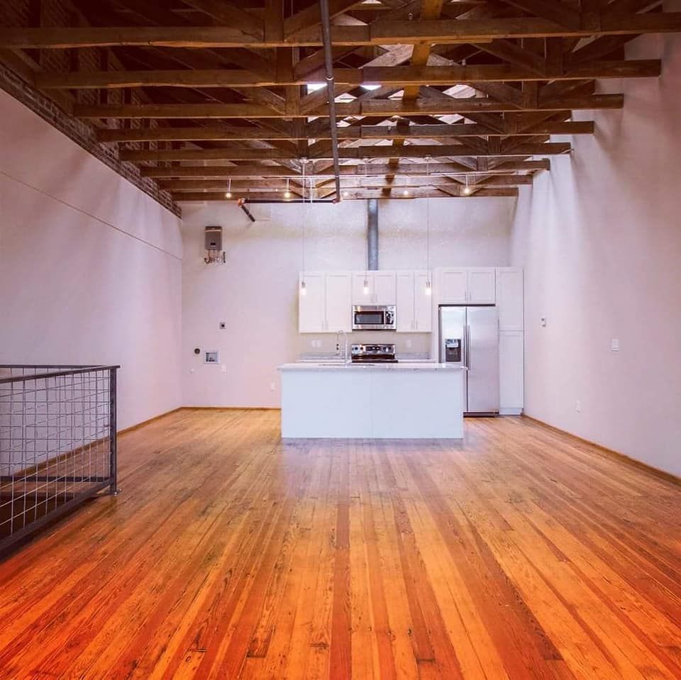 Open-concept living space with white kitchen island and appliances, hardwood floors, exposed wooden ceiling beams.