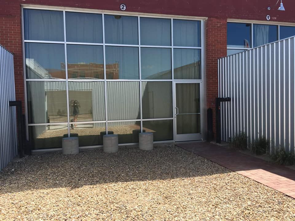 Building with large glass windows, gravel yard, metal siding, and concrete barriers.