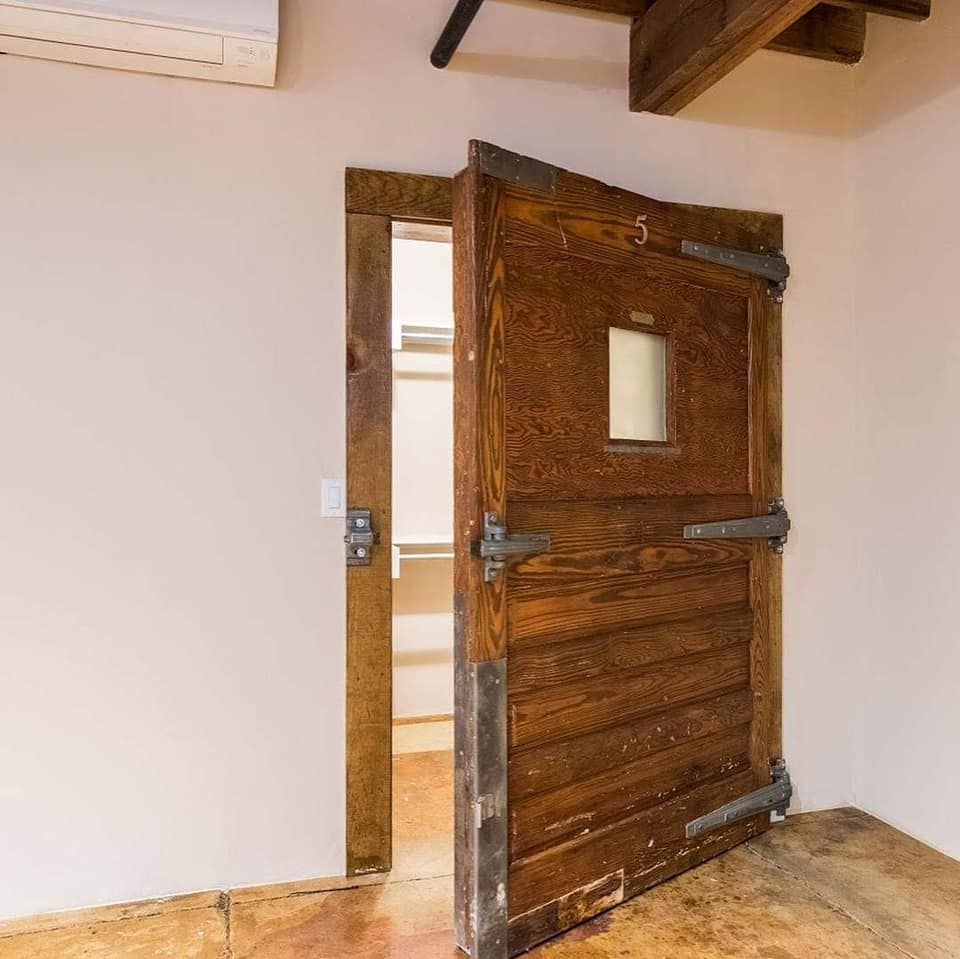 Wooden door, slightly ajar, revealing a closet. Dark brown wood, metal hinges, and a small window in the door.