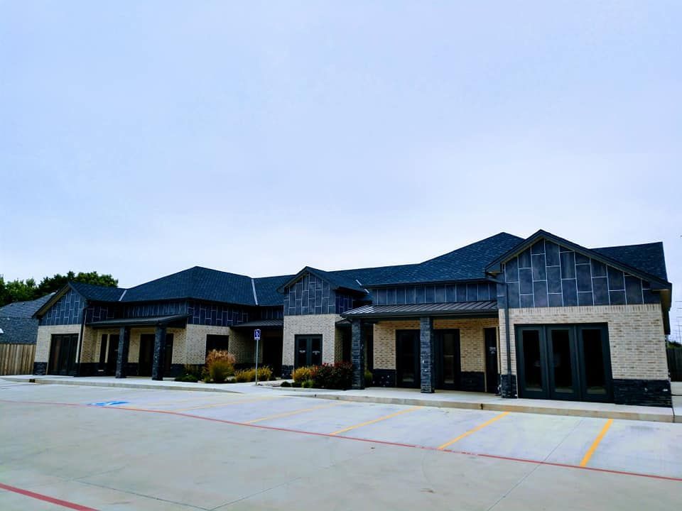 Row of tan brick buildings with black roofs and trim under a cloudy sky.