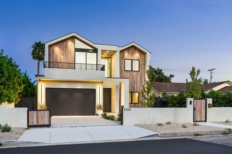 A modern two-story home at twilight, featuring light-colored walls, wood-paneled accents, a dark garage, and a gated yard.