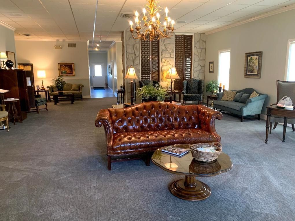 Cozy waiting area with brown leather sofa, teal couches, gold chandelier, and gray carpet.