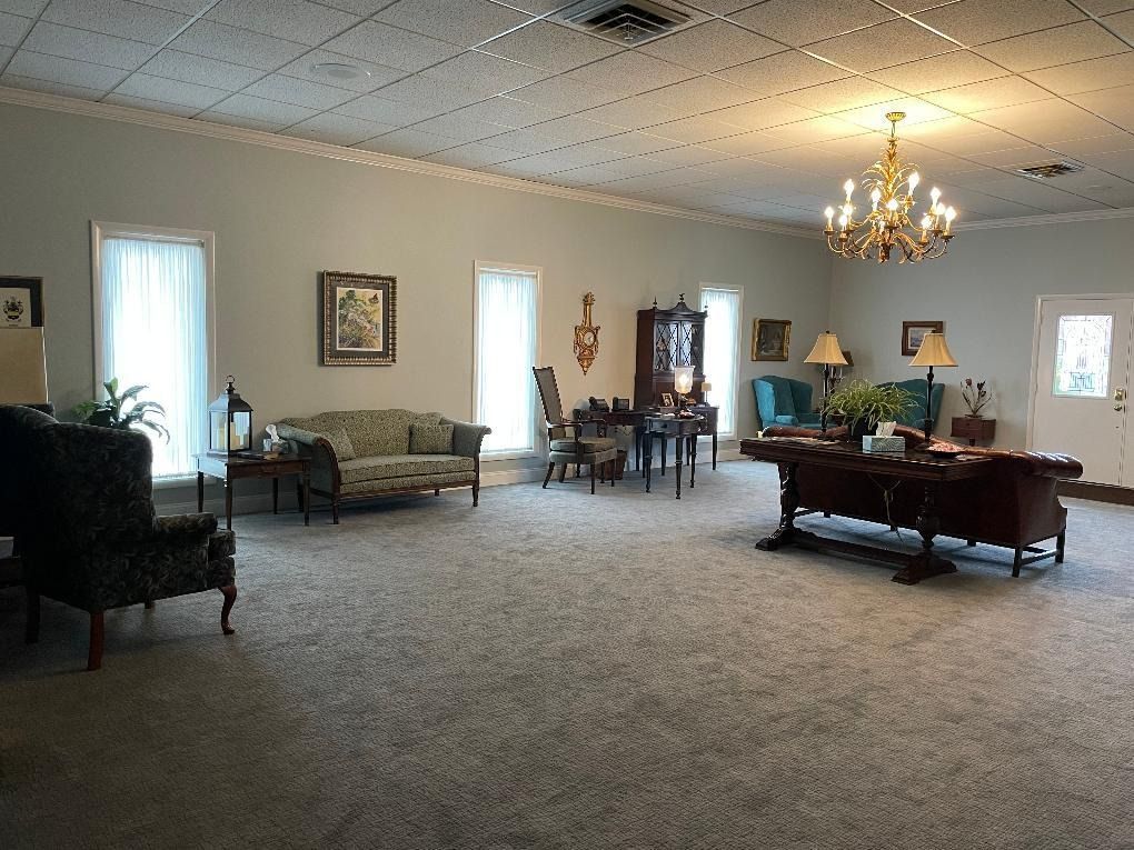Spacious room with furniture: sofas, chairs, tables, and a chandelier; neutral tones, likely a waiting area.