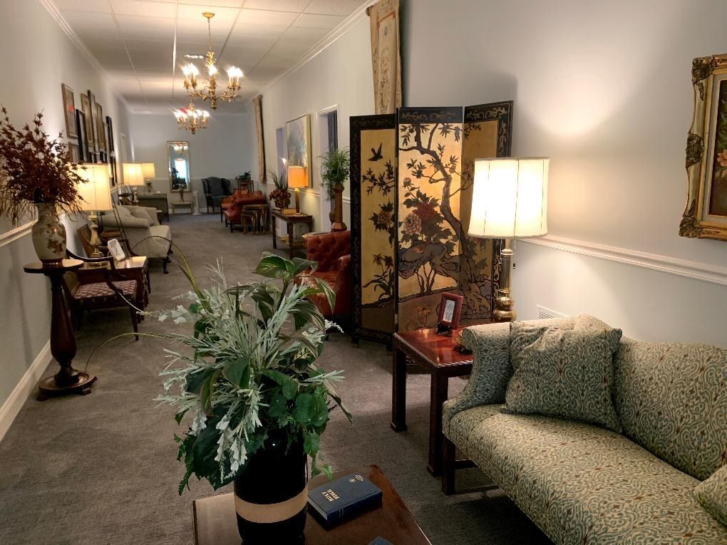 Long hallway with seating areas, lamps, and decorative screens. Pale blue walls, ornate trim, and carpeted floor.