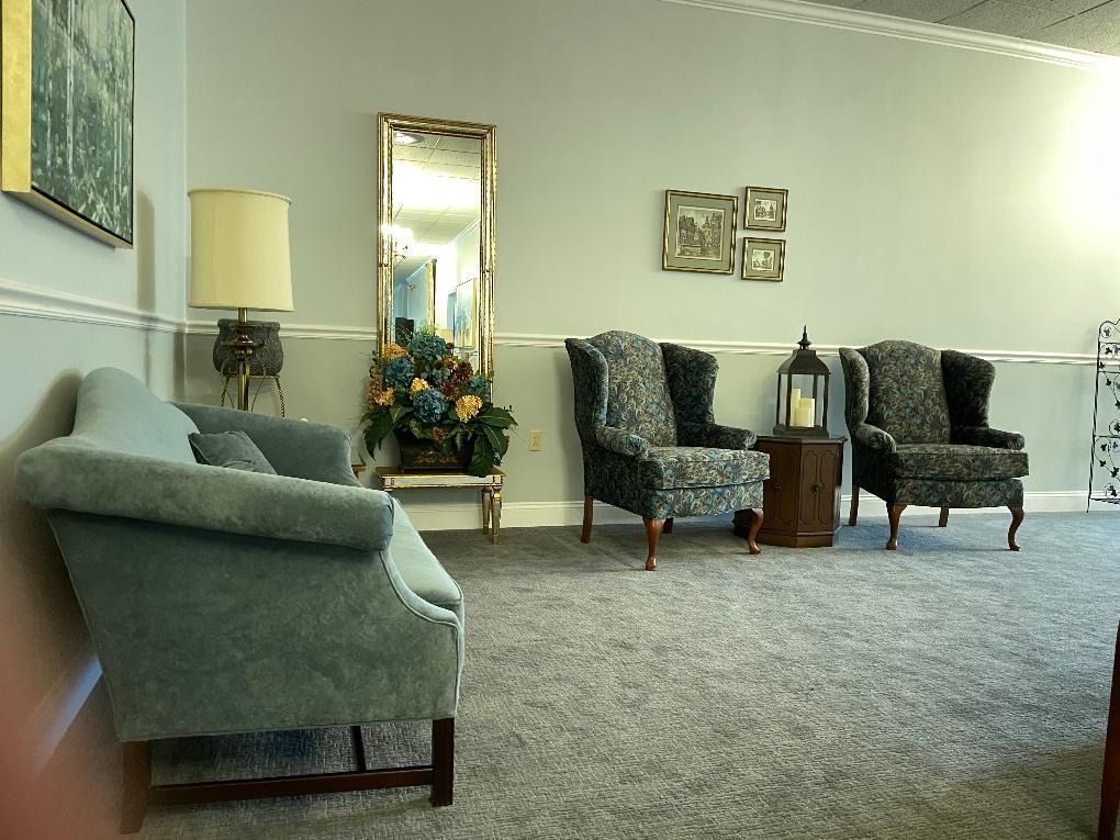 A waiting room with teal chairs, a mirror, and framed photos against light blue walls and gray carpet.