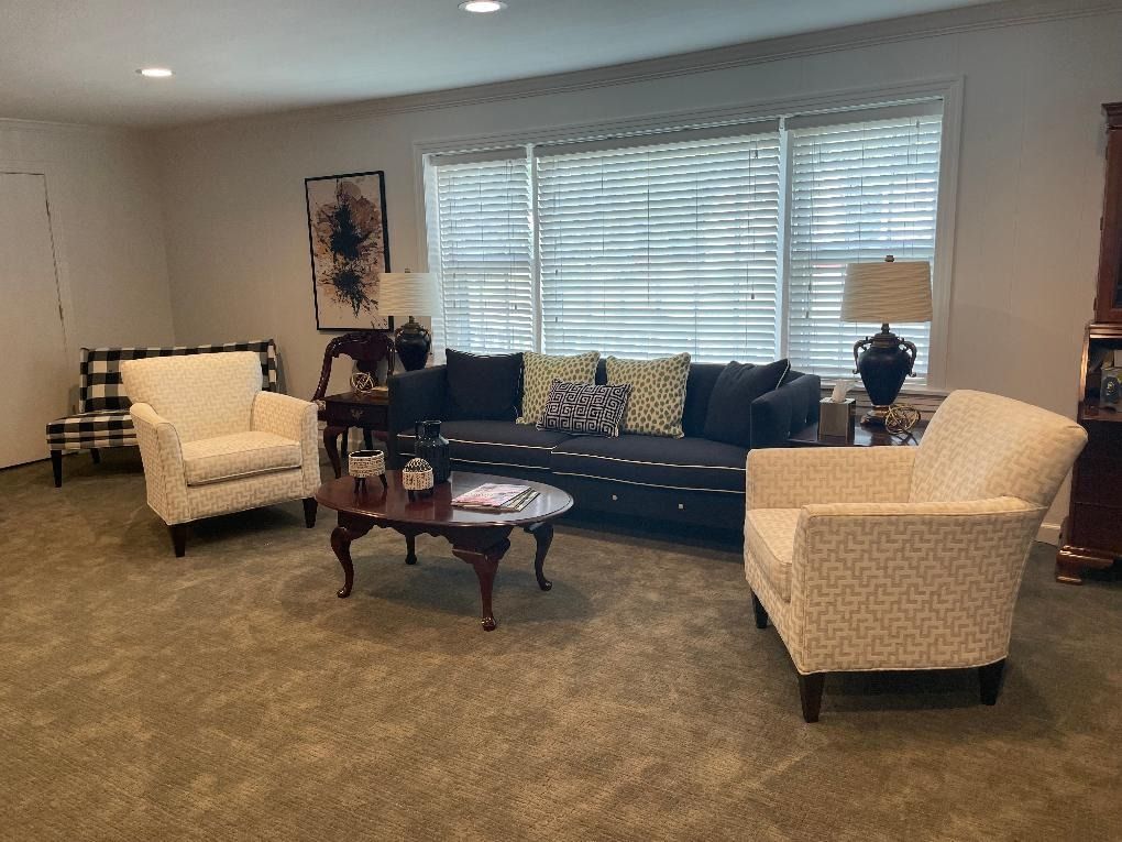 Living room with dark sofa, patterned chairs, coffee table, and window with blinds.
