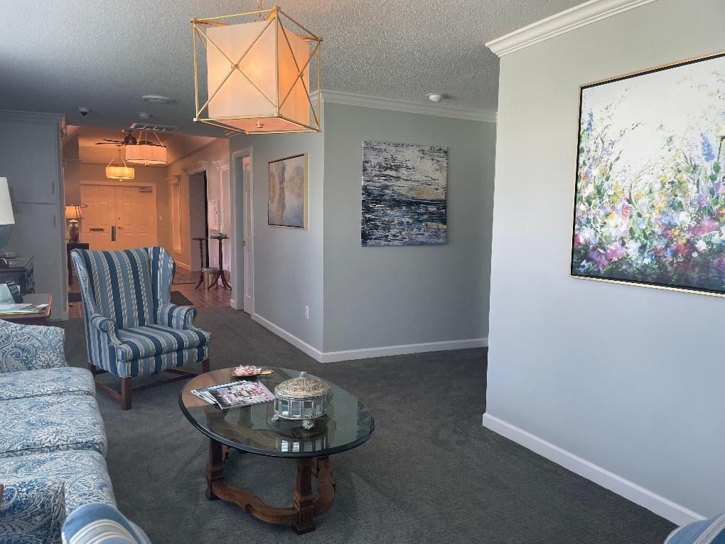 Living room with blue patterned furniture, glass table, and artwork on gray walls.