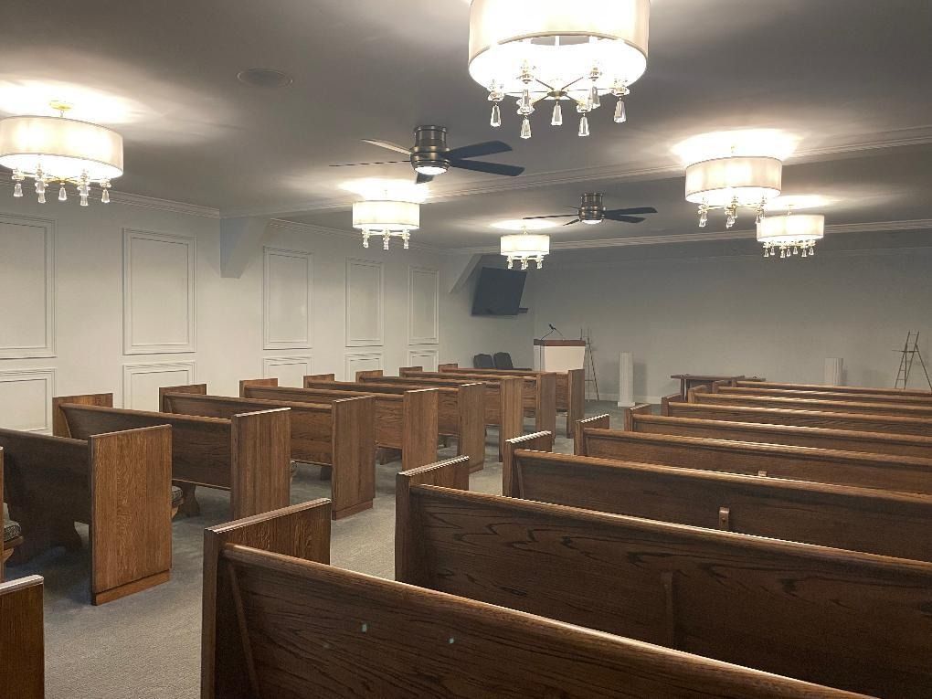 An empty church interior with rows of wooden pews, chandeliers, and ceiling fans.