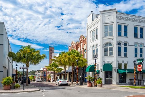 Sunny downtown street with palm trees, colorful storefronts, and white historic buildings under a blue sky