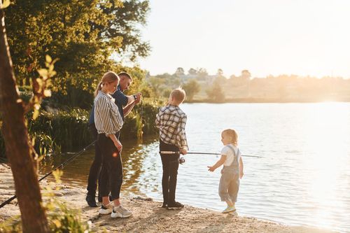 People standing by a lakeshore at sunset, watching a child near the water.