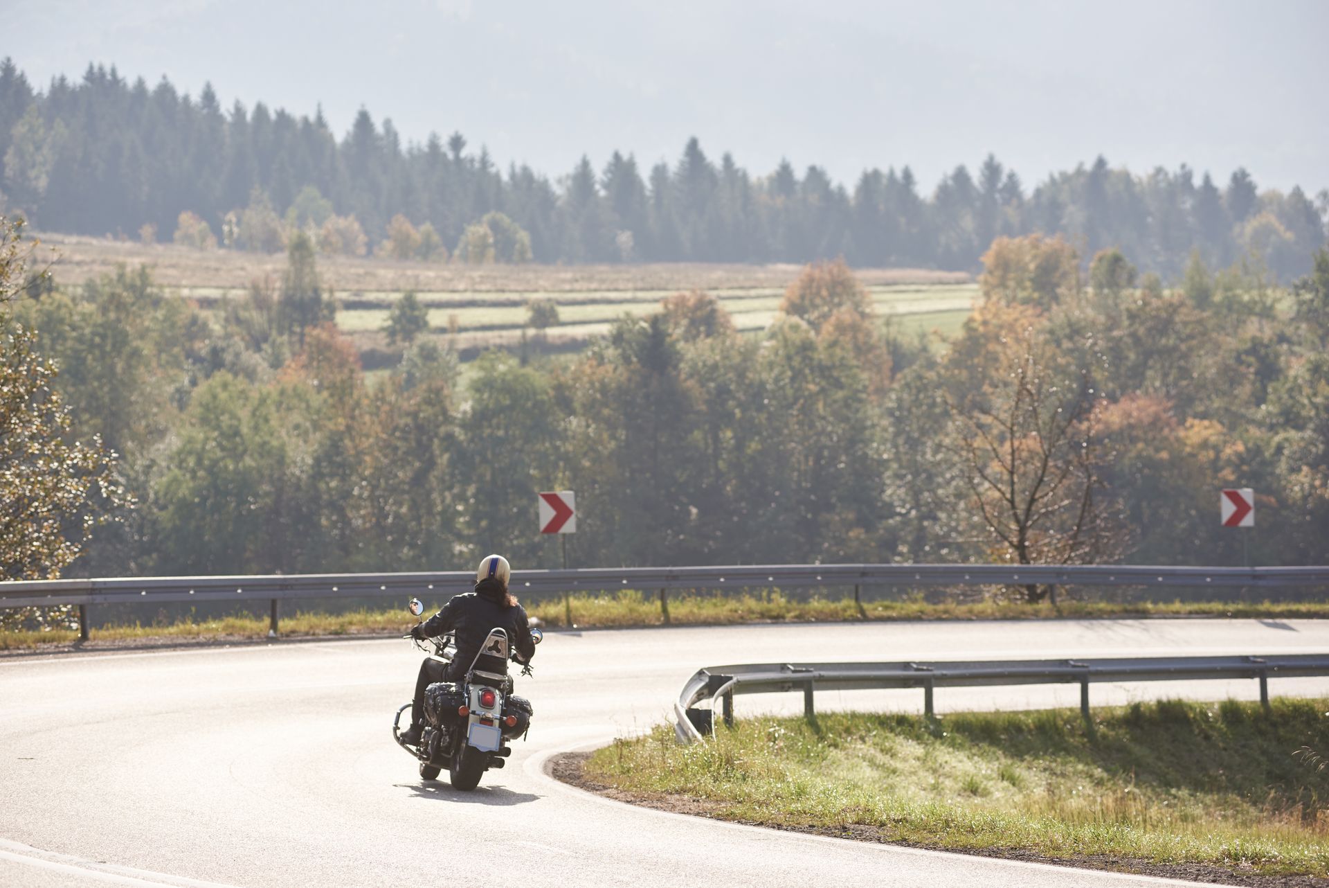 Motorcyclist leaning through a curving rural road with guardrails and autumn trees in the background