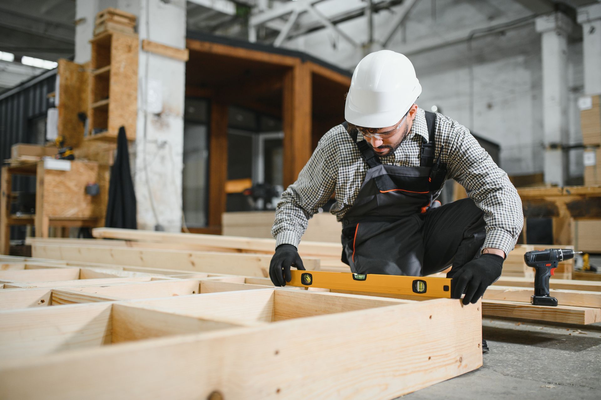 Worker in a hard hat using a power tool to cut a wooden beam in a workshop