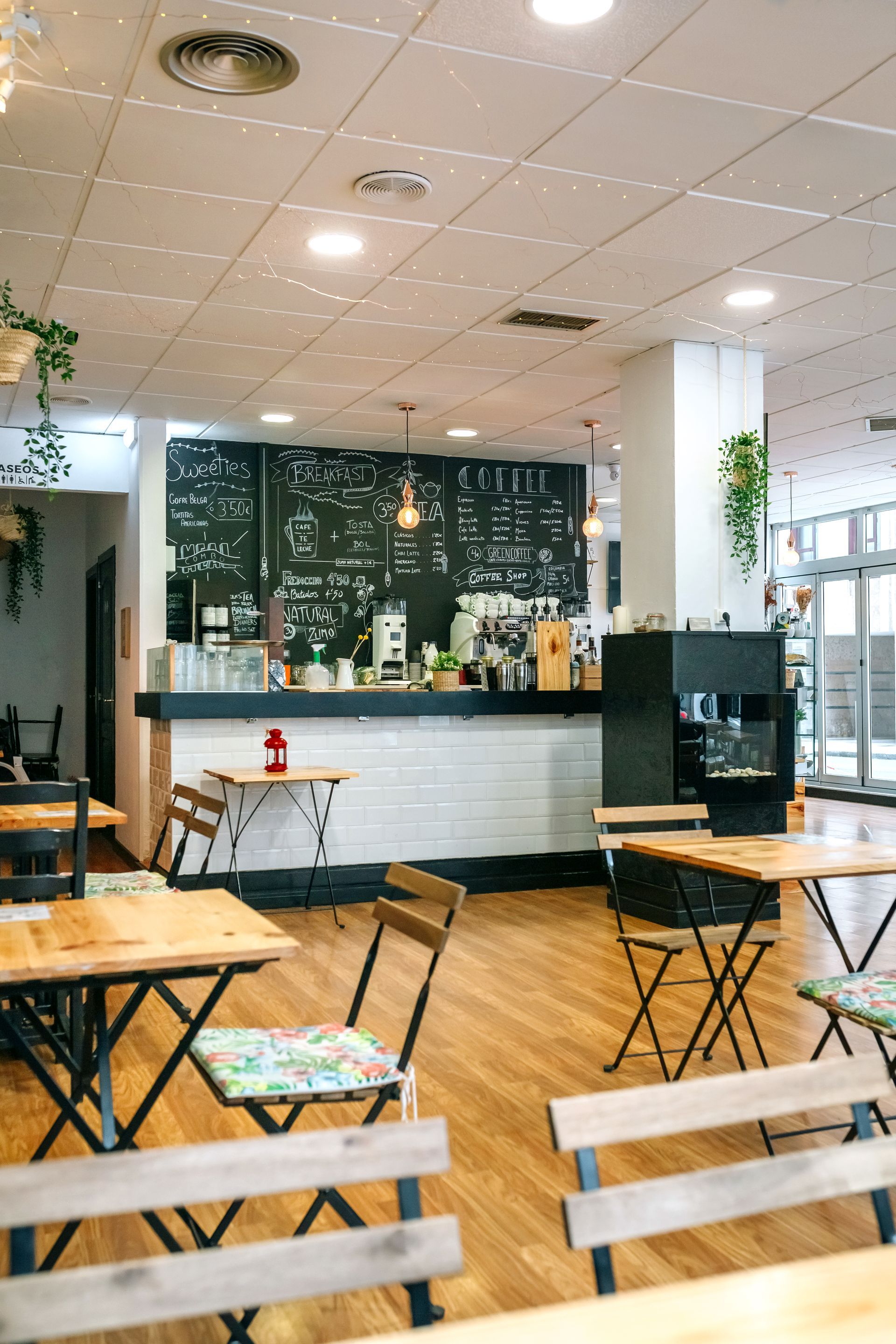 Bright café interior with wooden tables, black menu wall, and hanging plants