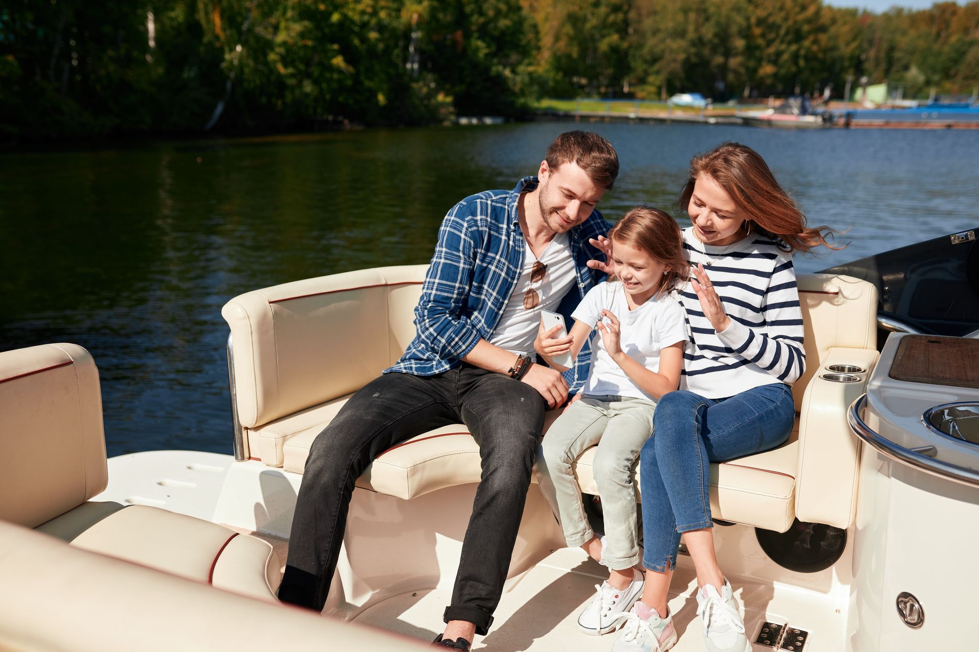 Three people sitting on a boat bench, smiling by the water on a sunny day