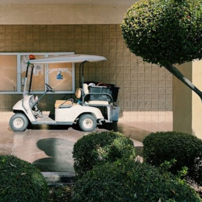 White golf cart parked by a tiled wall with trimmed bushes in the foreground