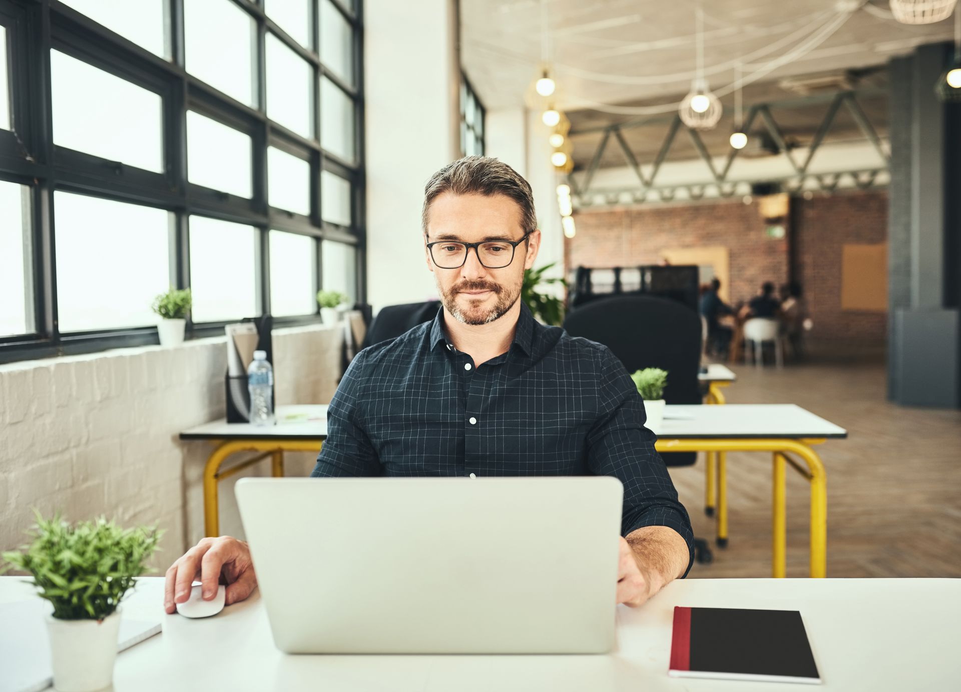 Man sitting at a laptop in a bright modern office with large windows and plants