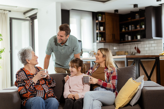Family chatting in a living room, with a man standing by a couch beside two women and a child.